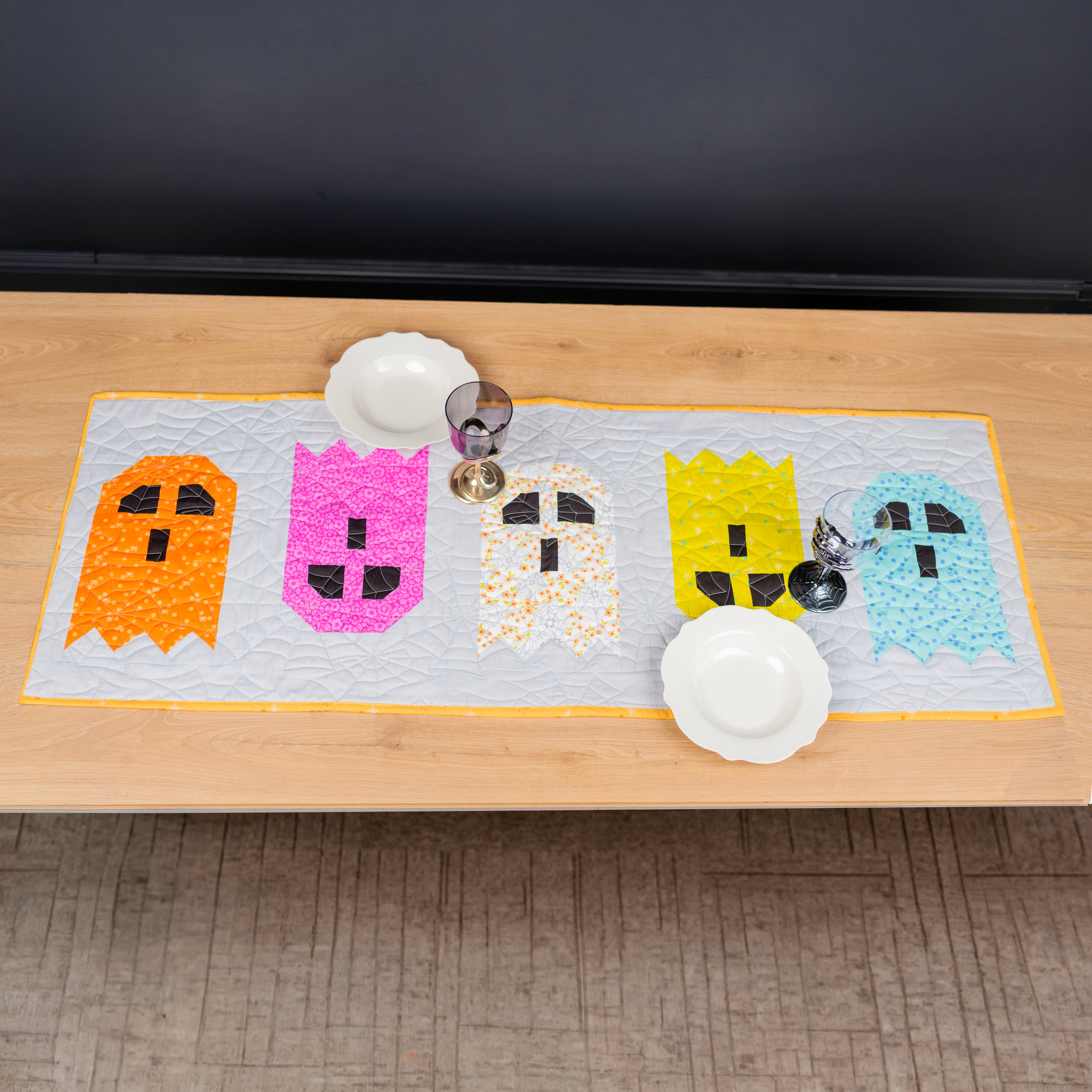 Five colorful ghosts on a table runner.