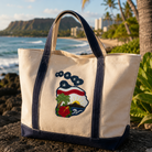 Beige tote bag with a tropical design on a stone surface with ocean and palm trees in the background