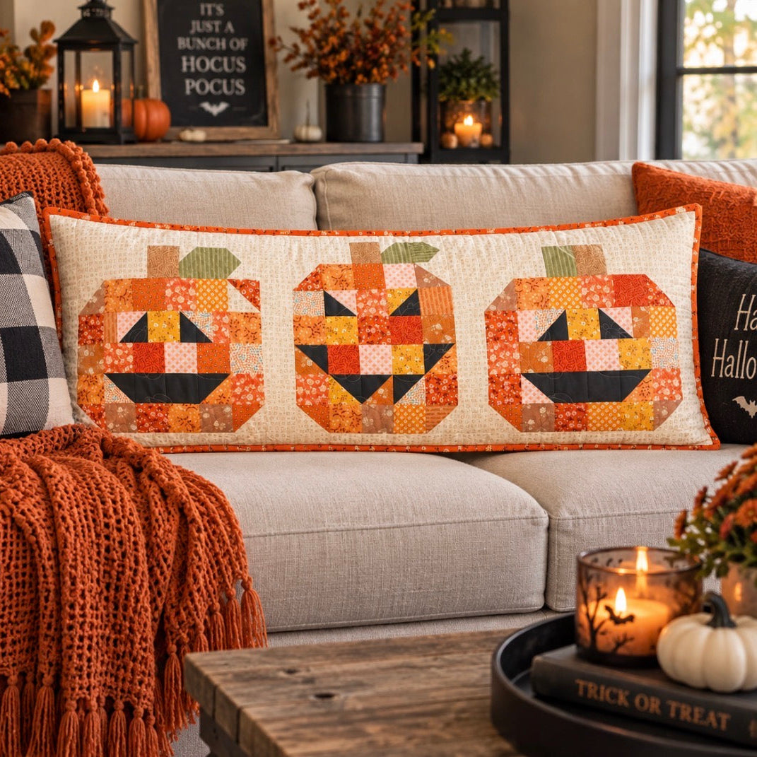 A rectangular patchwork pumpkin bench pillow with three carved jack-o'-lantern faces sits on a dark wooden porch bench. The pillow features a cream background with orange, yellow, black, and green patchwork pumpkin designs.