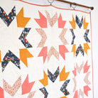 Quilt with geometric pattern featuring triangles in orange, pink, and blue on a white background.