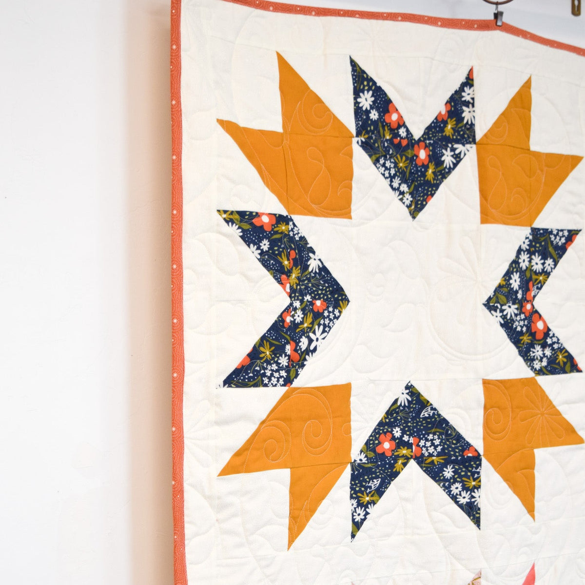 Quilt with star pattern featuring orange, blue, and pink colors on a white background