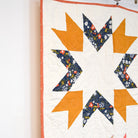 Quilt with star pattern featuring orange, blue, and pink colors on a white background