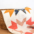 Quilt with colorful geometric patterns draped over a wicker basket on a wooden floor.