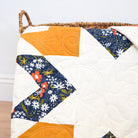 Quilt with star pattern featuring orange, blue, and white fabric on a wooden surface.
