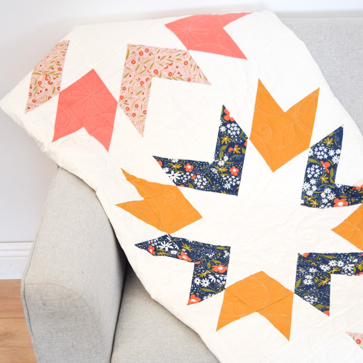 Colorful arrow-patterned quilt draped over a gray armchair.