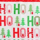 A close-up of a quilted fabric featuring a festive 'HO HO HO' holiday pattern with red and green text and Christmas tree motifs on a white background.