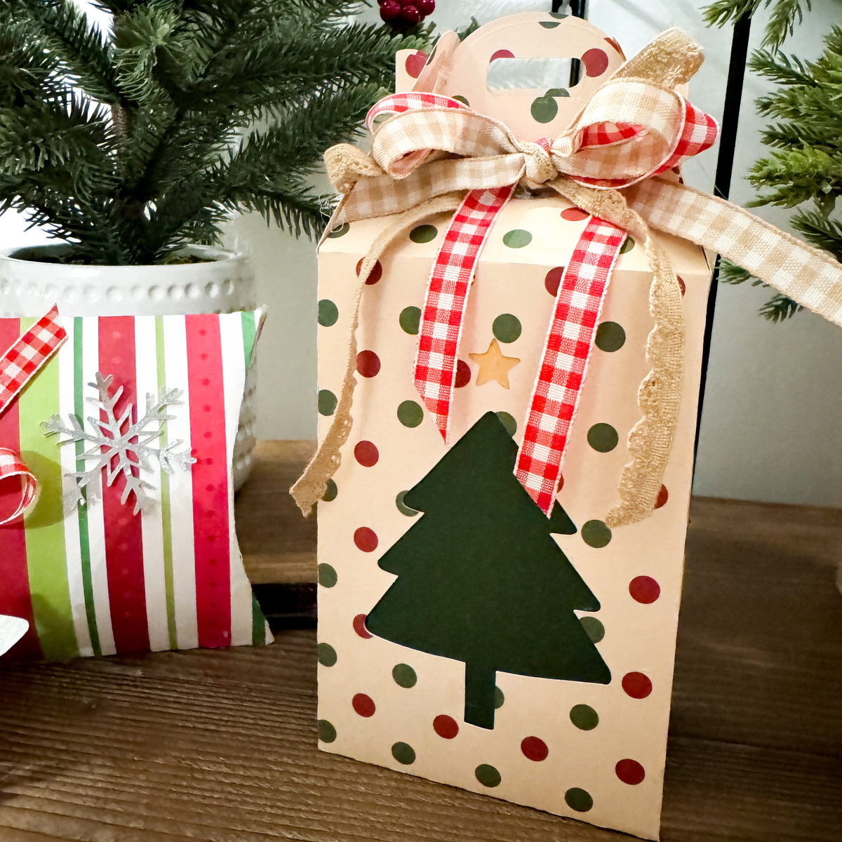 Decorative gift bag with polka dots and Christmas tree design, tied with a ribbon, in front of a Christmas tree.