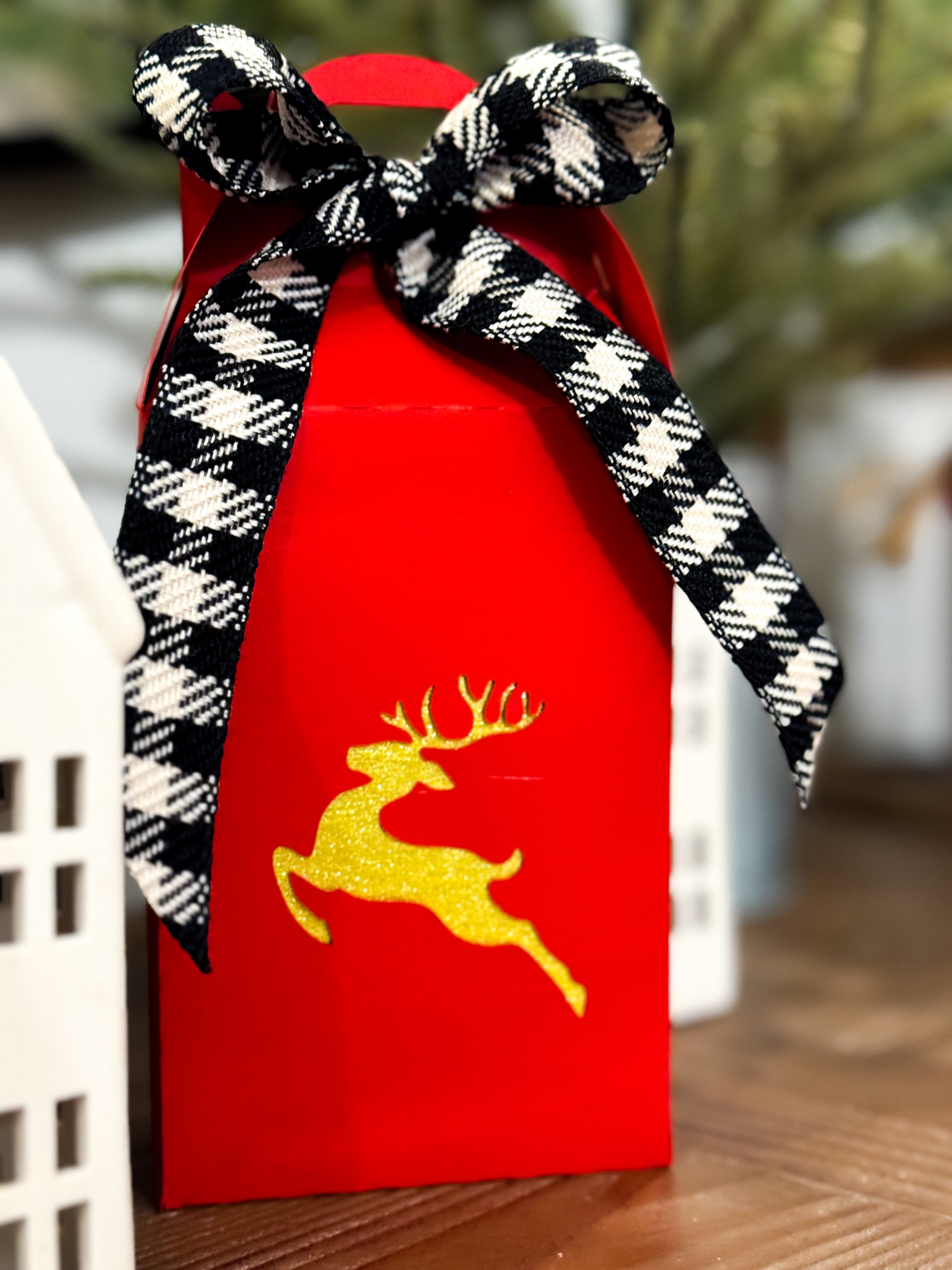 Red gift bag with a black and white checkered bow and gold deer design on a blurred background