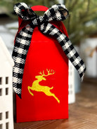 Red gift bag with a black and white checkered bow and gold deer design on a blurred background