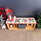 Decorative table runner with red berries and green leaves on a wooden console table against a dark wall.