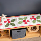 Decorative table runner with red and green patterns on a wooden table against a dark wall.