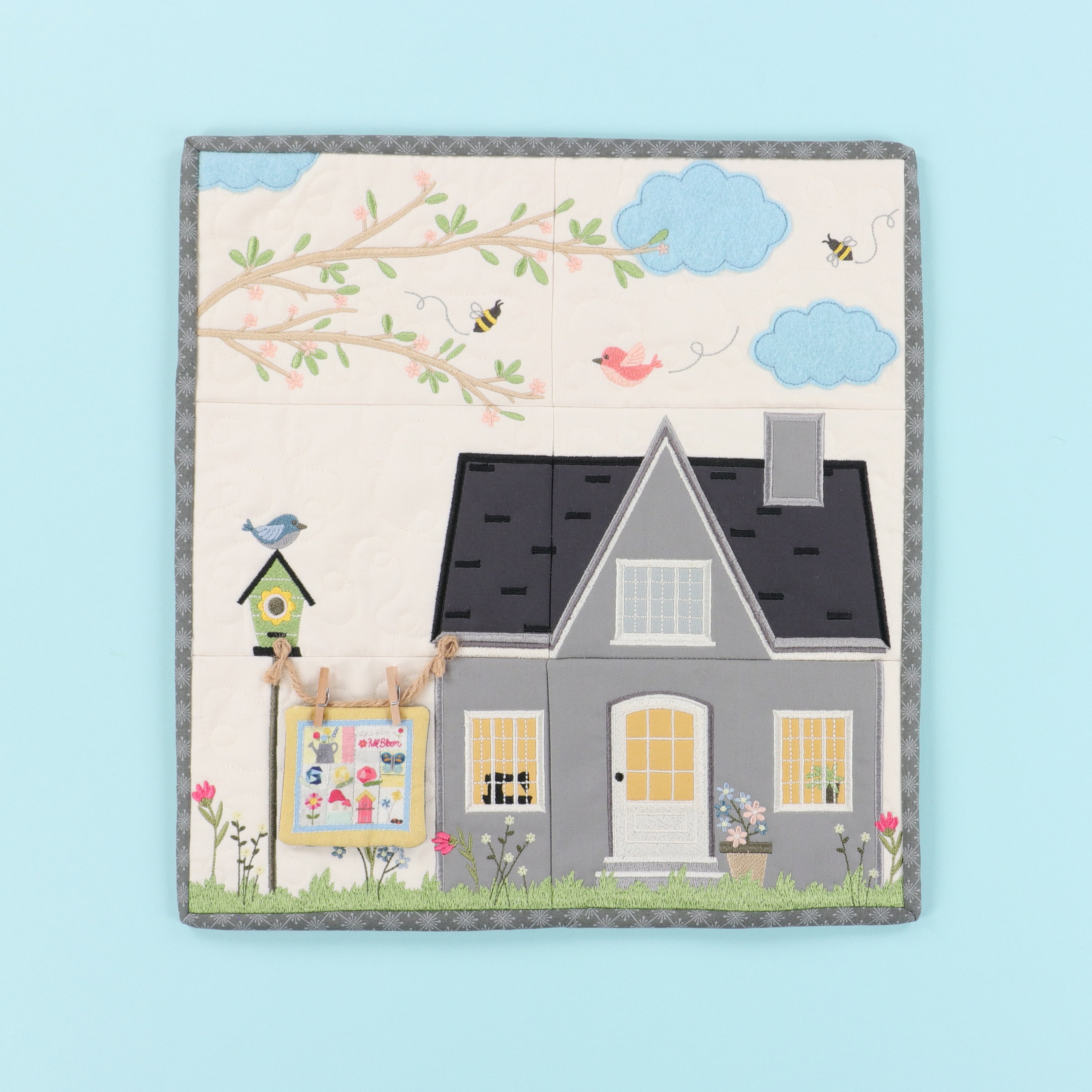 Children's quilt with a house, tree, and birds on a light blue background