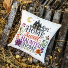 A square white decorative throw pillow with a colorful embroidered 'Home Sweet Haunted Home' design, placed on a rustic wooden pallet outdoors.