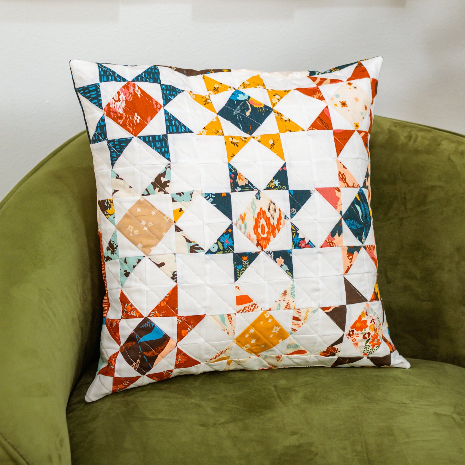 Patchwork pillow with multicolor patterns on a green armchair.