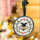 A circular honeybee-themed bag tag with embroidery detailing, held against a blurred background.