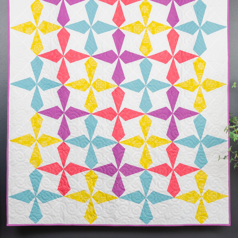 Colorful geometric quilt on a gray wall with a smaller floral quilt on a ladder.