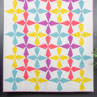 Colorful geometric quilt on a gray wall with a smaller floral quilt on a ladder.