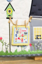 Children's quilt with a birdhouse, flowers, and a small house on a wooden surface.