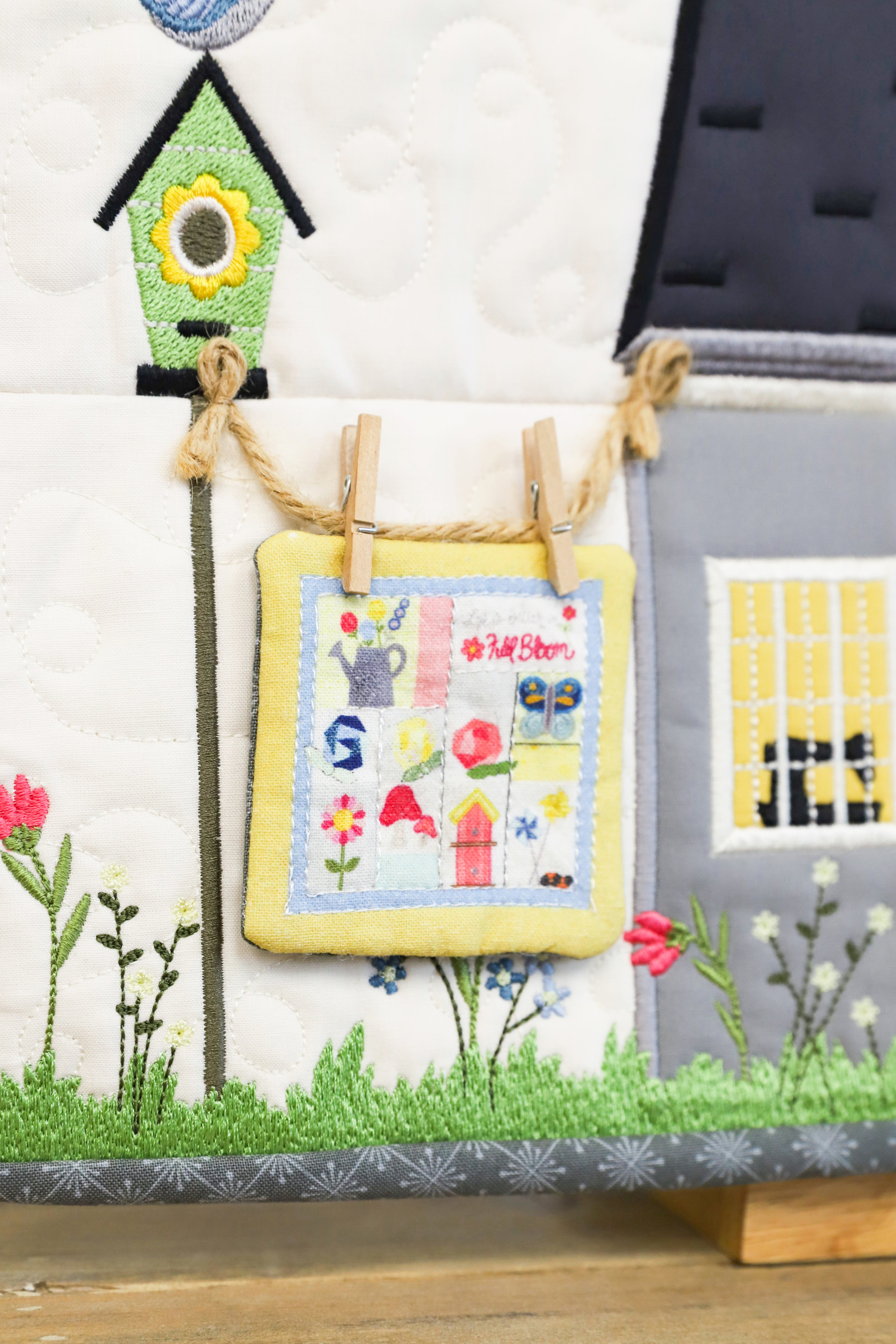 Children's quilt with a birdhouse, flowers, and a small house on a wooden surface.