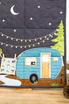Quilt with a camper design, trees, and string lights against a night sky.