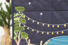 Navy blue quilt with embroidered green tree, white stars, and yellow lights on a dark background.