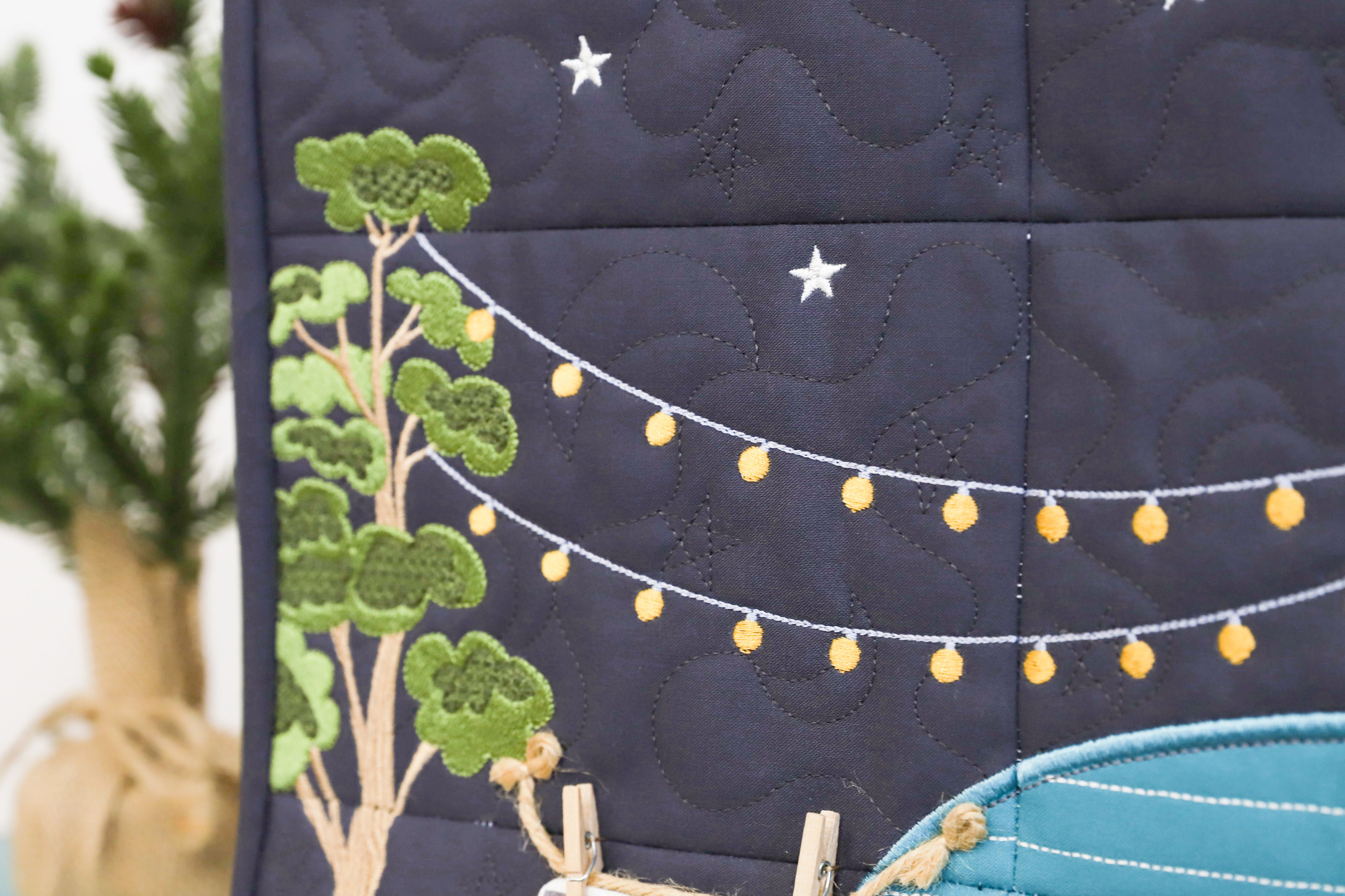 Navy blue quilt with embroidered green tree, white stars, and yellow lights on a dark background.
