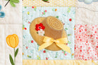 Quilt block with a straw hat, flowers, and a yellow bow on a floral background