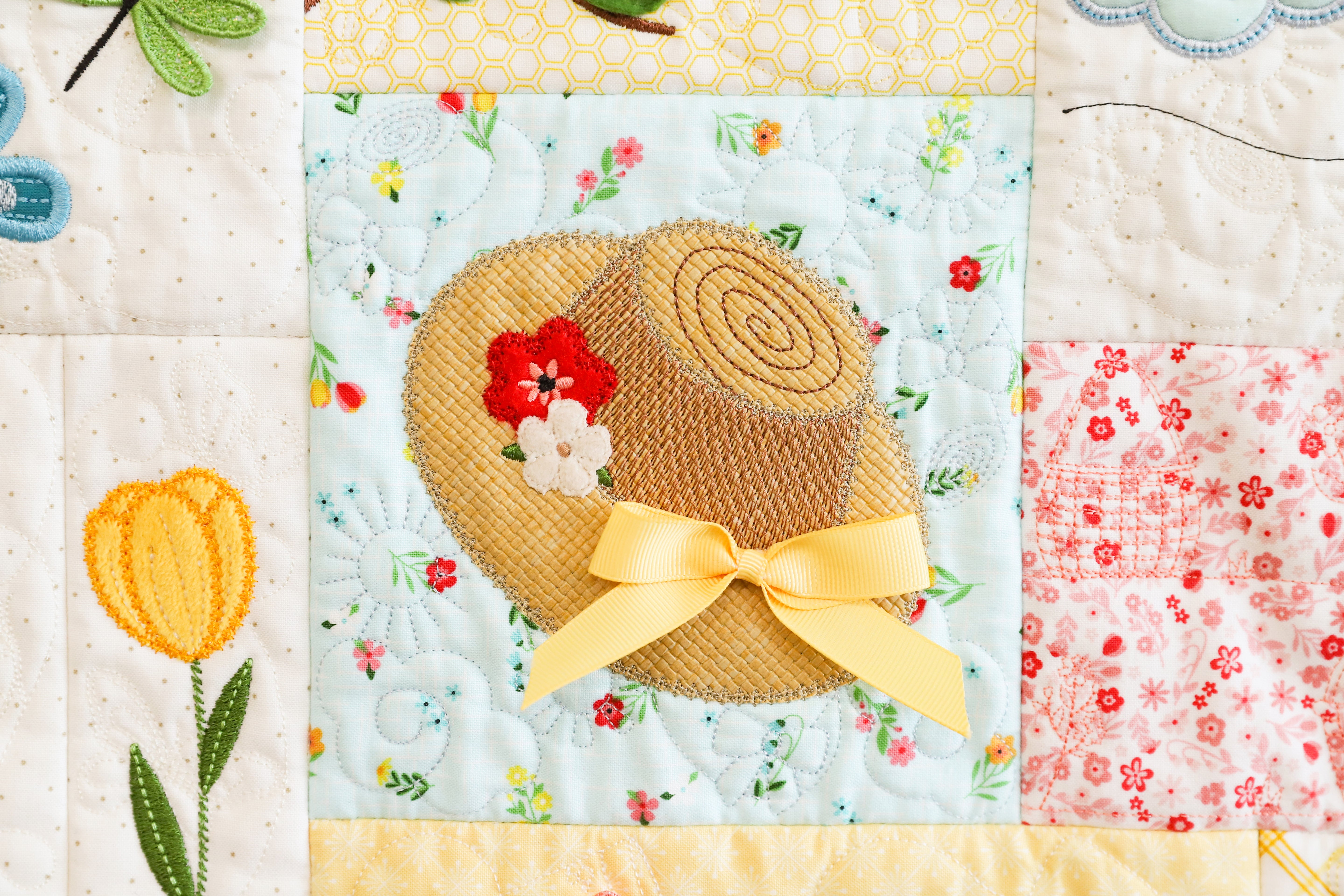 Quilt block with a straw hat, flowers, and a yellow bow on a floral background