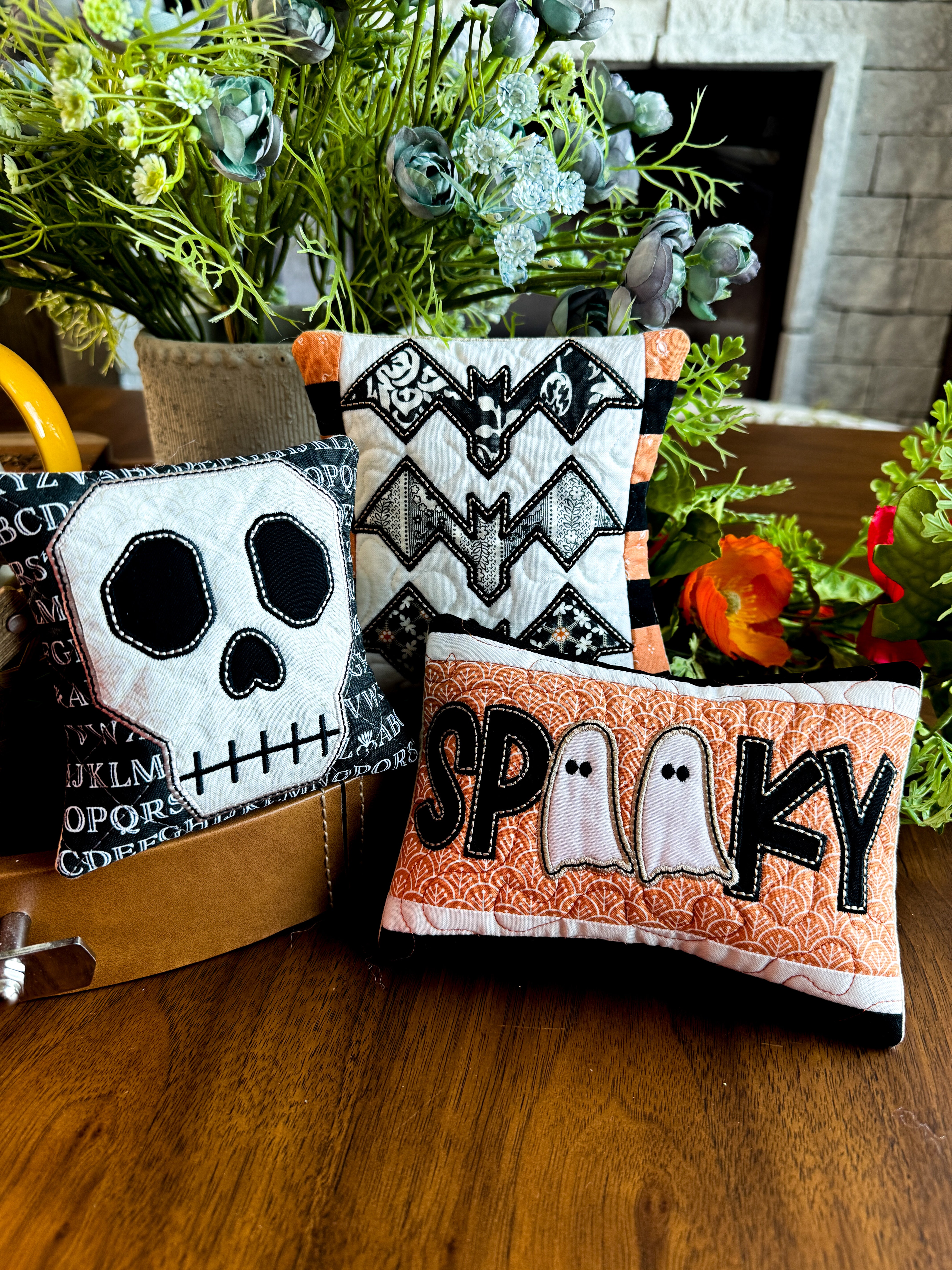 Three Halloween-themed decorative pillows on a wooden surface with plants in the background.