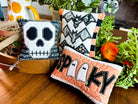 Halloween-themed decorative pillows on a wooden surface with plants in the background