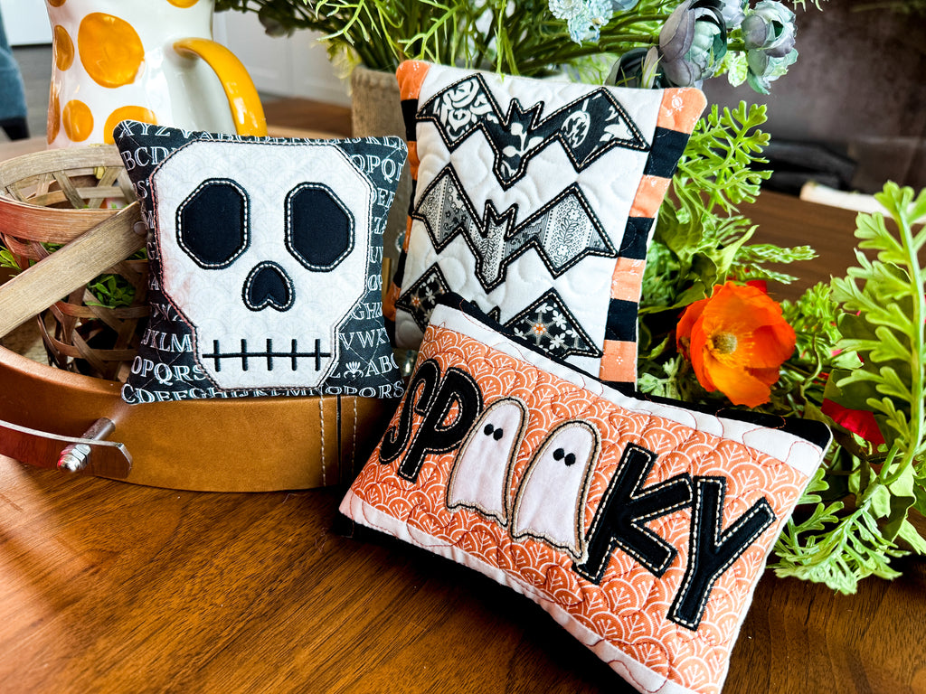 Halloween-themed decorative pillows on a wooden surface with plants in the background