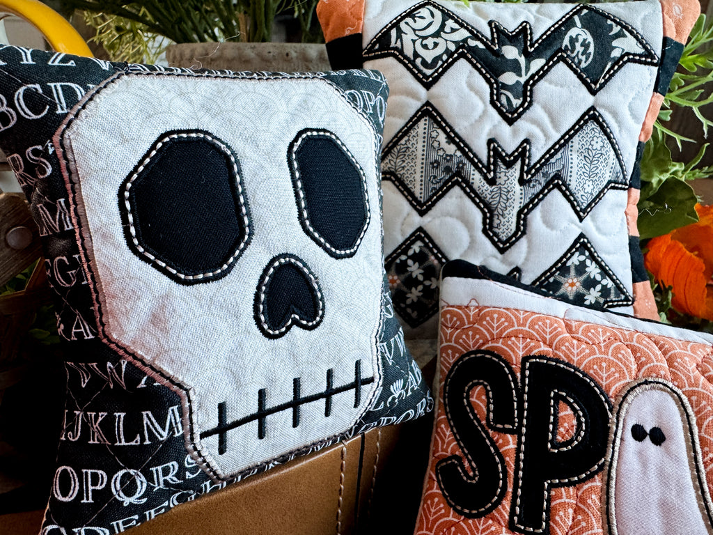 Halloween-themed decorative pillows with skull, bat, and ghost designs.