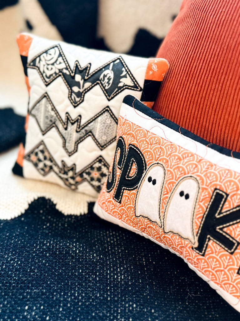 Decorative pillows with Halloween-themed designs on a textured surface.