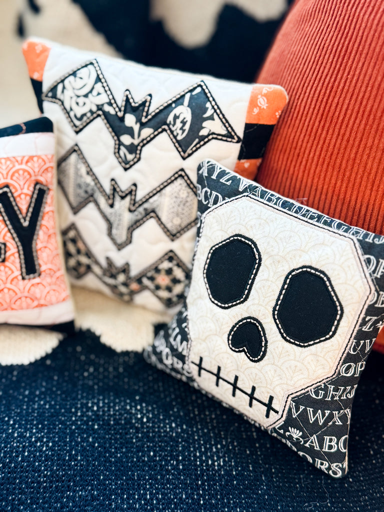 Decorative pillows with Halloween-themed designs on a textured surface.