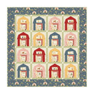 A square quilt or patchwork artwork featuring a grid of small barn-like houses in red, pink, yellow, and blue, surrounded by a blue border with tiny farmhouse motifs.
