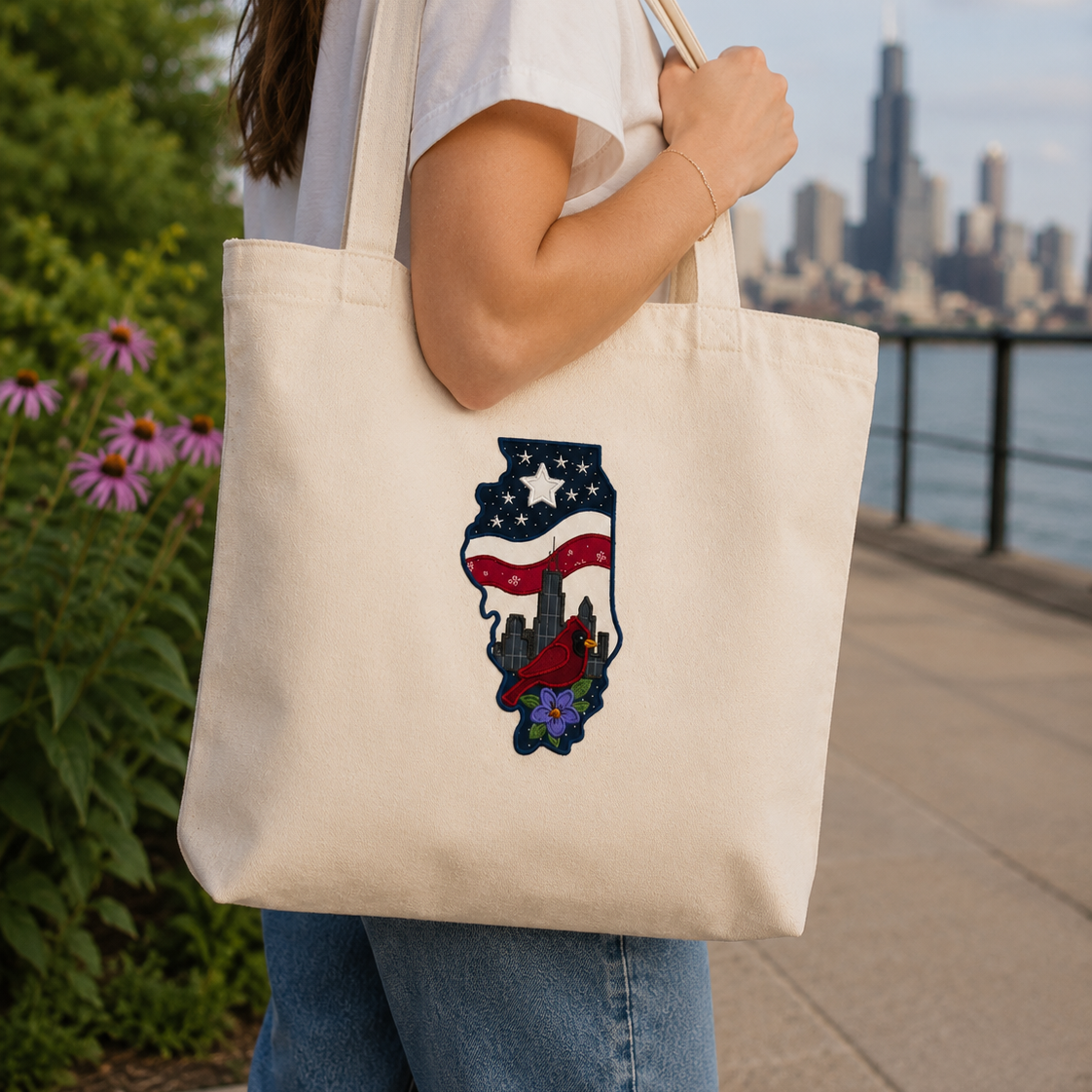Person holding a tote bag with a design of a city skyline and American flag, with a cityscape and water body in the background.
