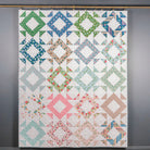 Colorful quilt with geometric patterns hanging on a gray wall.