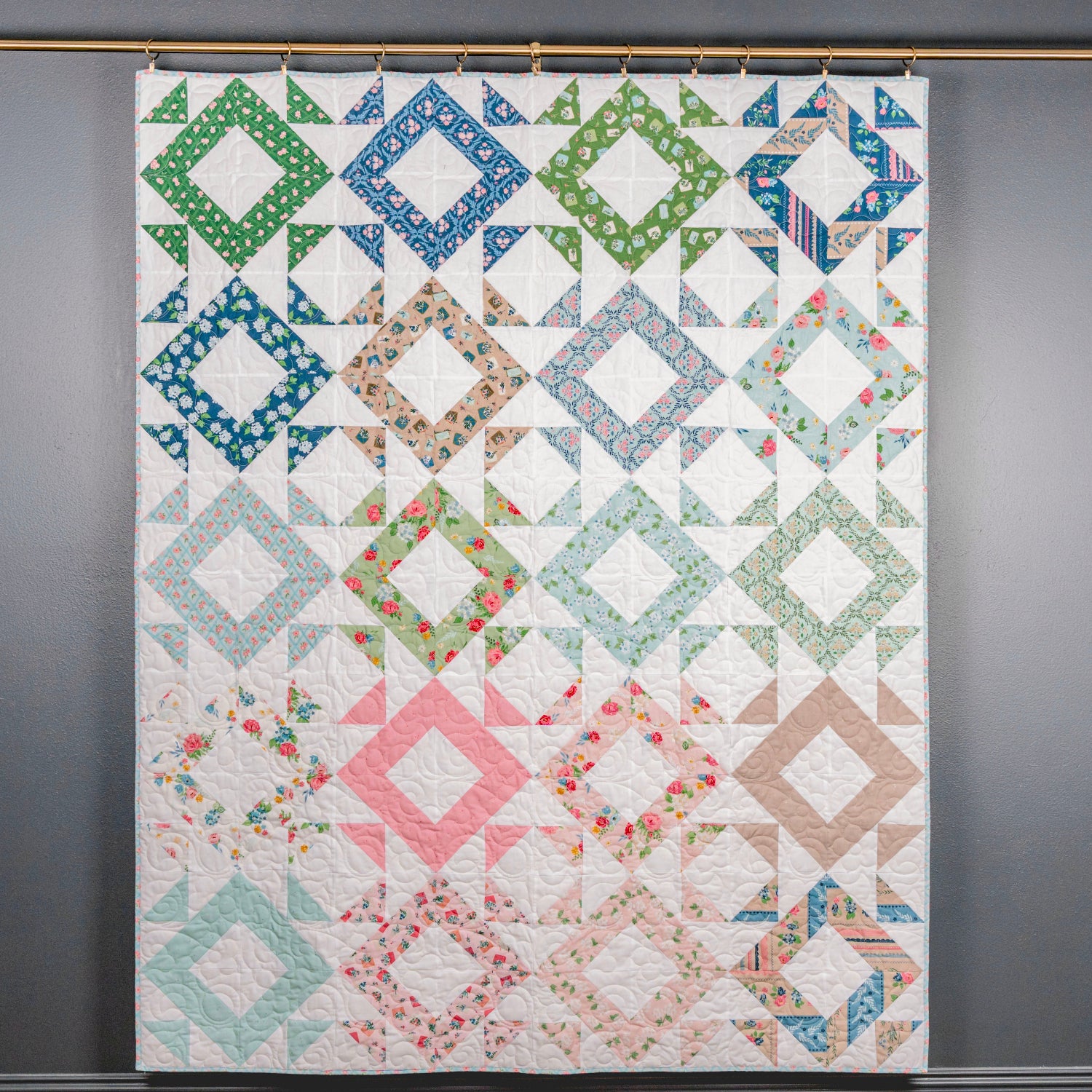 Colorful quilt with geometric patterns hanging on a gray wall.