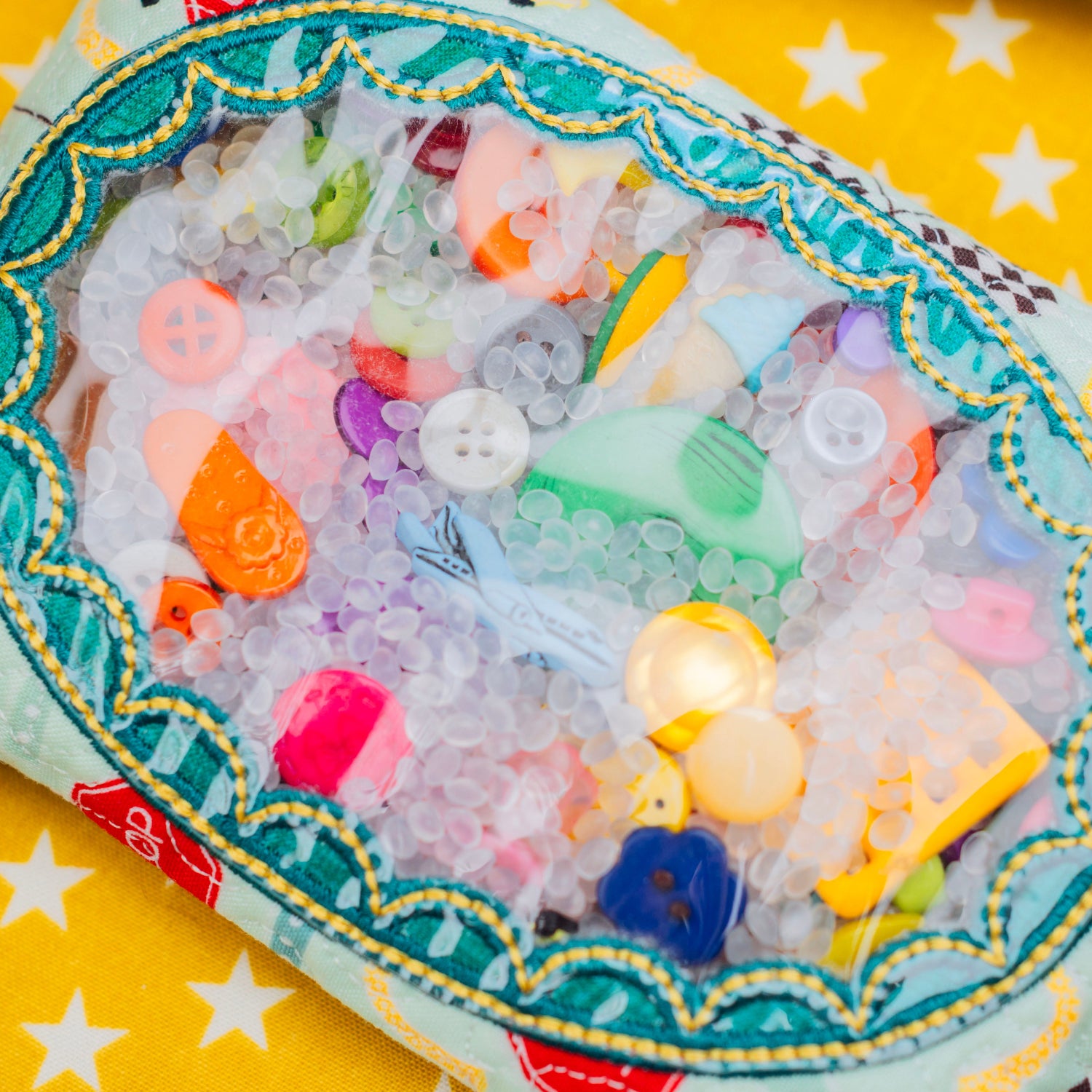 Colorful buttons and beads in a decorative container on a yellow background with star patterns