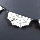 White bat-shaped bunting banner with black spiderweb patterns and small black spiders on a dark textured background.