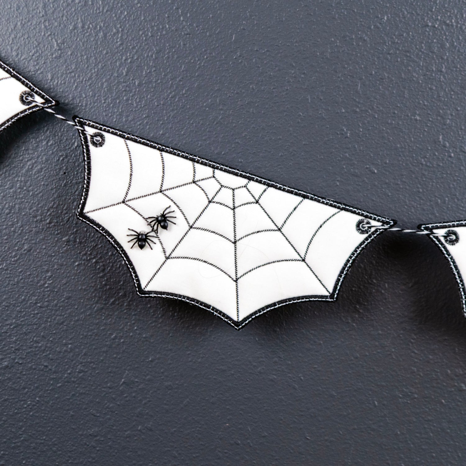 White bat-shaped bunting banner with black spiderweb patterns and small black spiders on a dark textured background.
