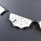 White bat-shaped banner flags with black spiderweb patterns and small black spider details, hanging against a dark gray textured background.