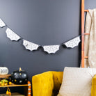 A styled interior corner with a mustard yellow armchair, white pillow, dark charcoal wall, spiderweb banner, small wooden side table with Halloween decor, and a wooden ladder leaning against the wall.