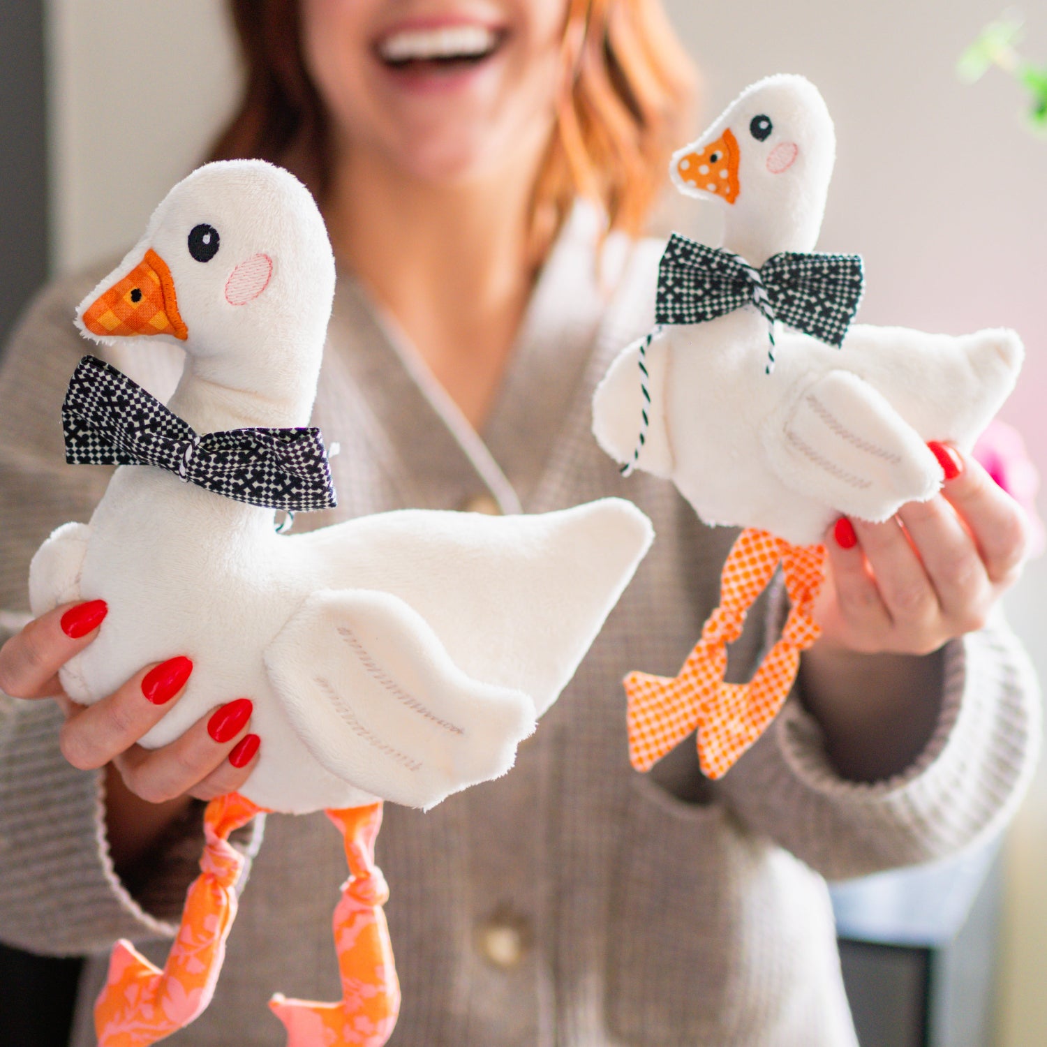 Person holding two plush ducks with bow ties in a home setting