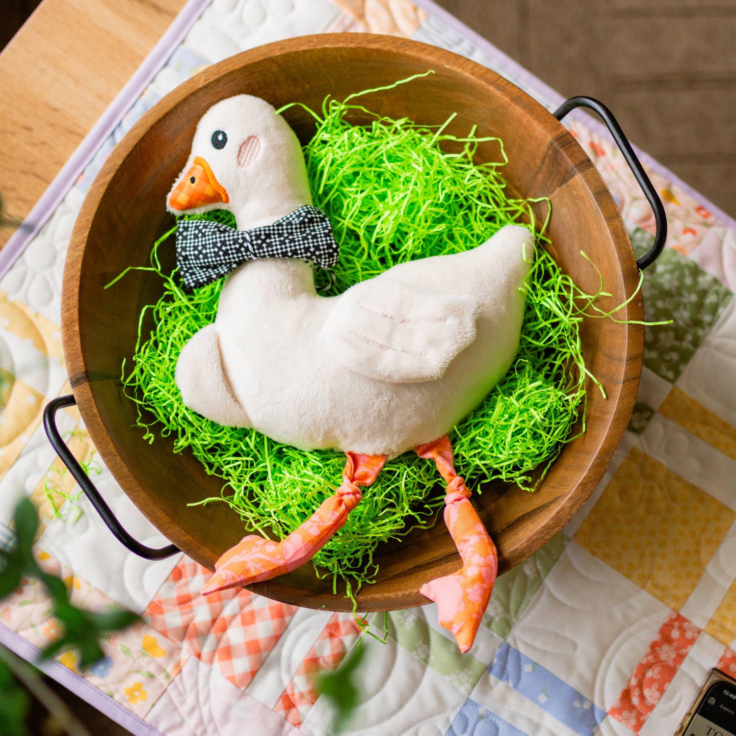 Decorative goose figurine with a bow tie in a wooden bowl on a patterned tablecloth.