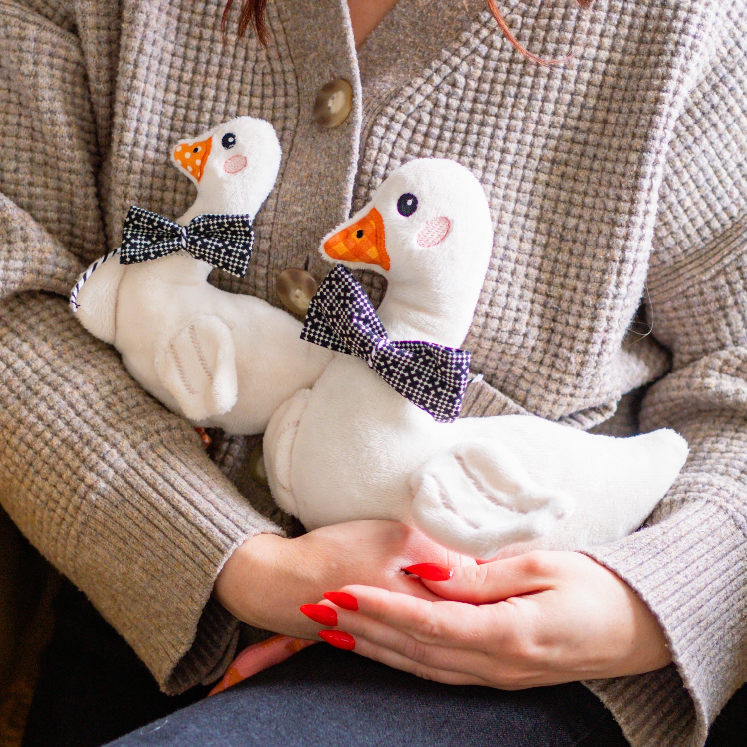 Person holding two white stuffed ducks with black bow ties in their hands.