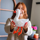 Woman holding a white goose-shaped pillow in a room with decor elements.