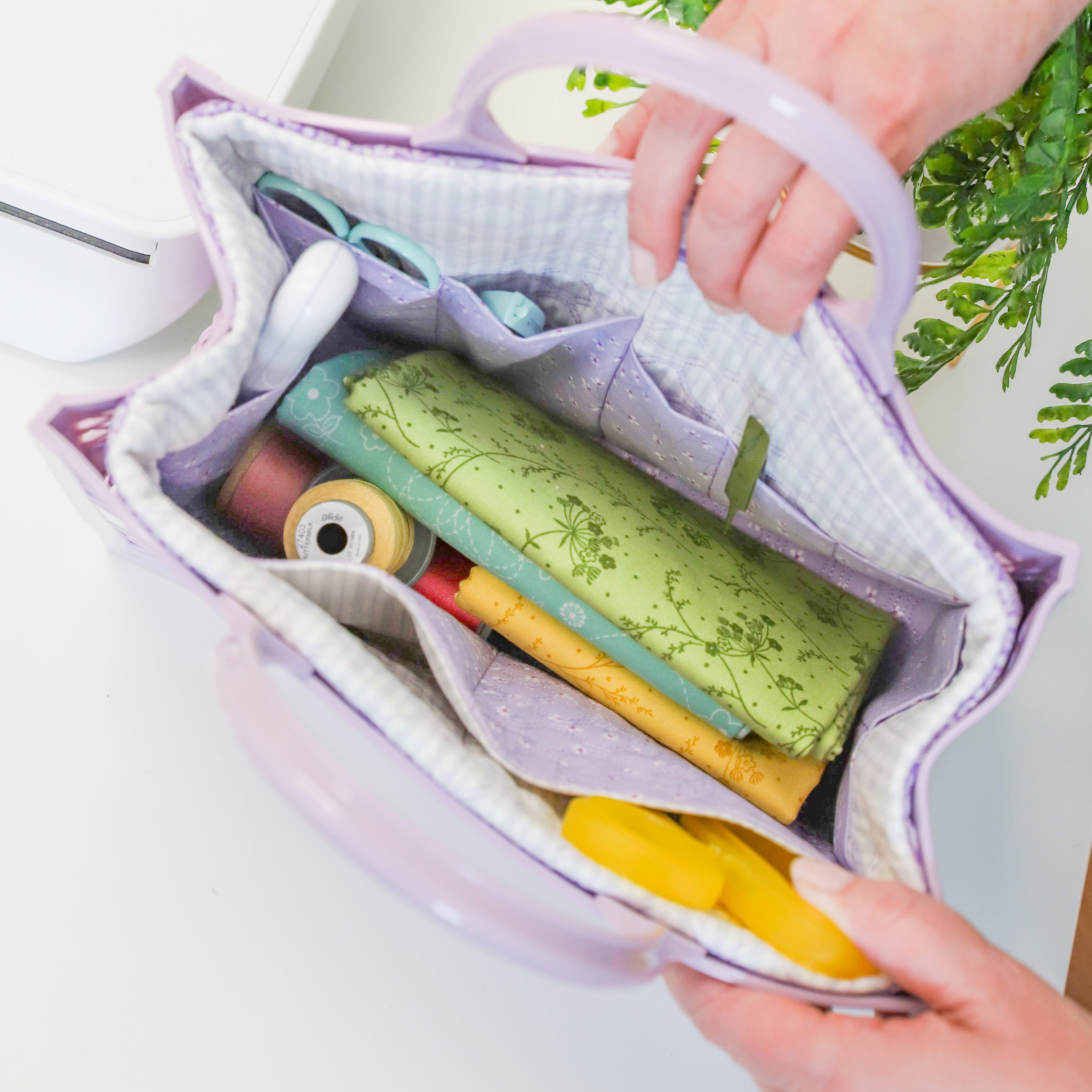 Purple bag with rolled-up items on a white surface with greenery in the background