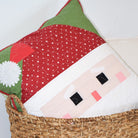 Decorative pillow with a Santa face design in a woven basket against a white wall.