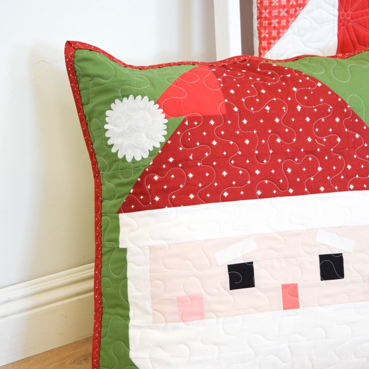 Quilted pillow with Santa Claus face design on a wooden floor.